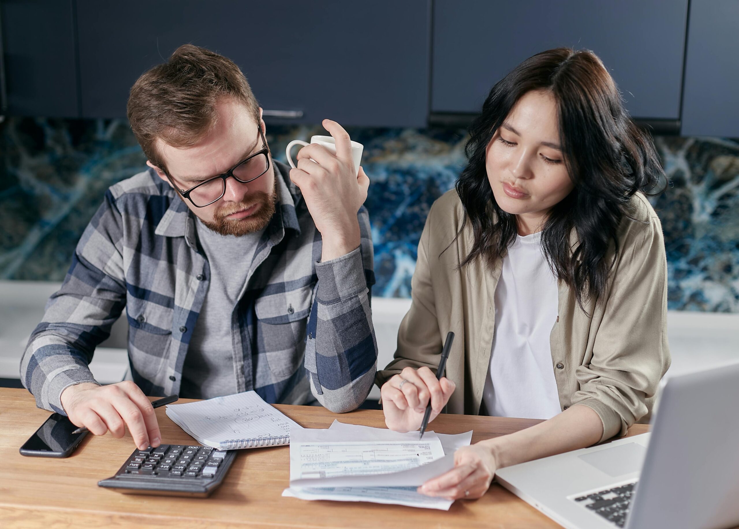 couple sitting at their desk reviewing finances with pen, paper, and calculator in front to understand good debt versus bad debt